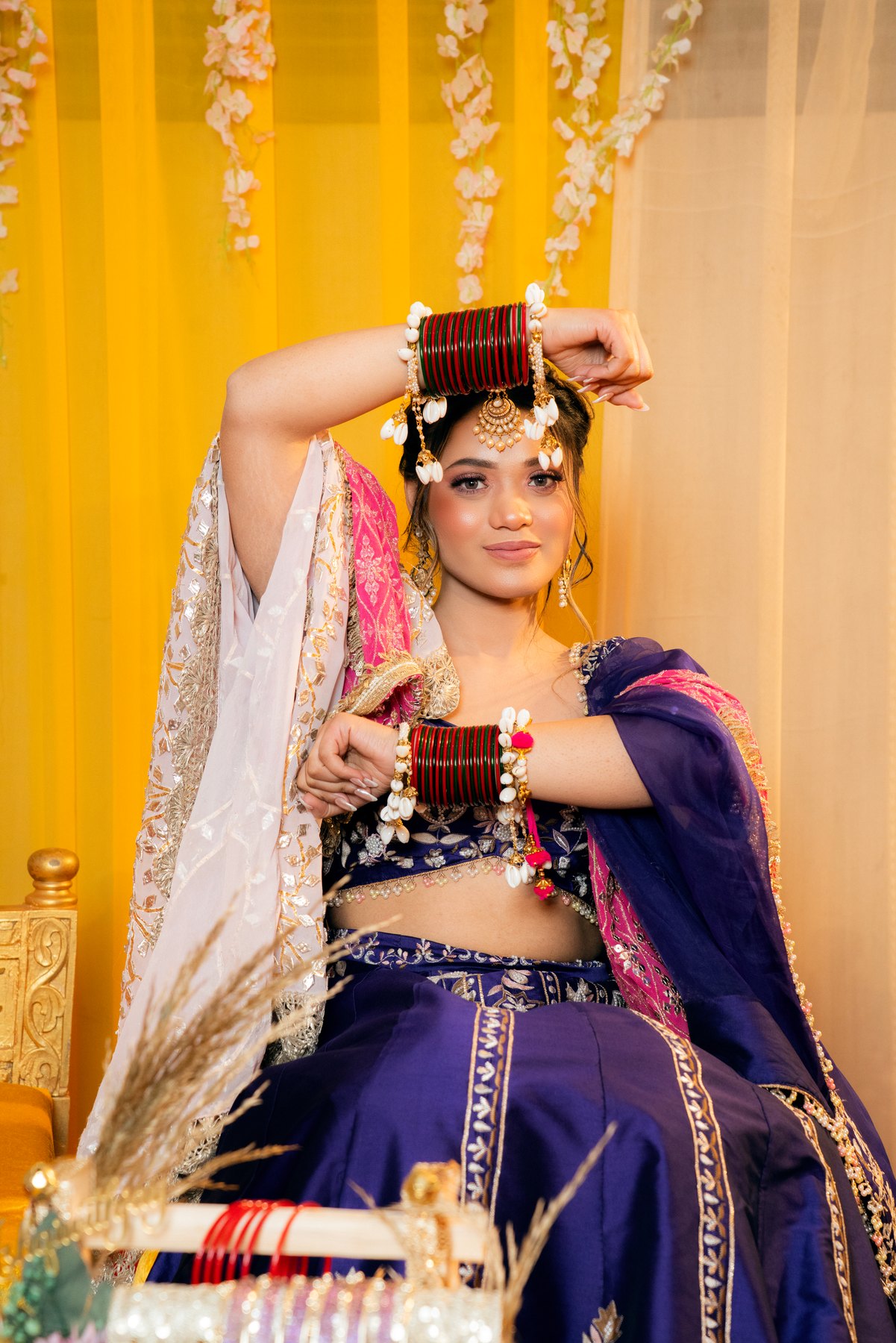 A bride in purple raising her bangled hands against warm yellow drapes