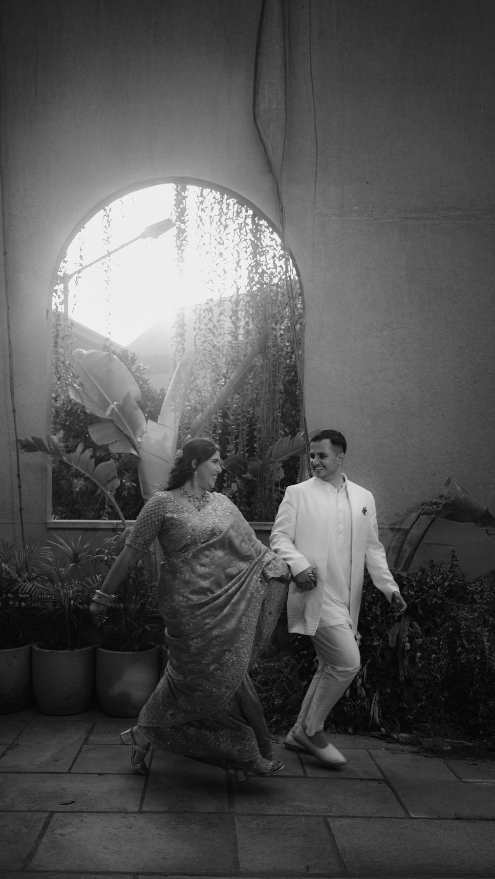 A black-and-white couple portrait beside a sunlit arched window