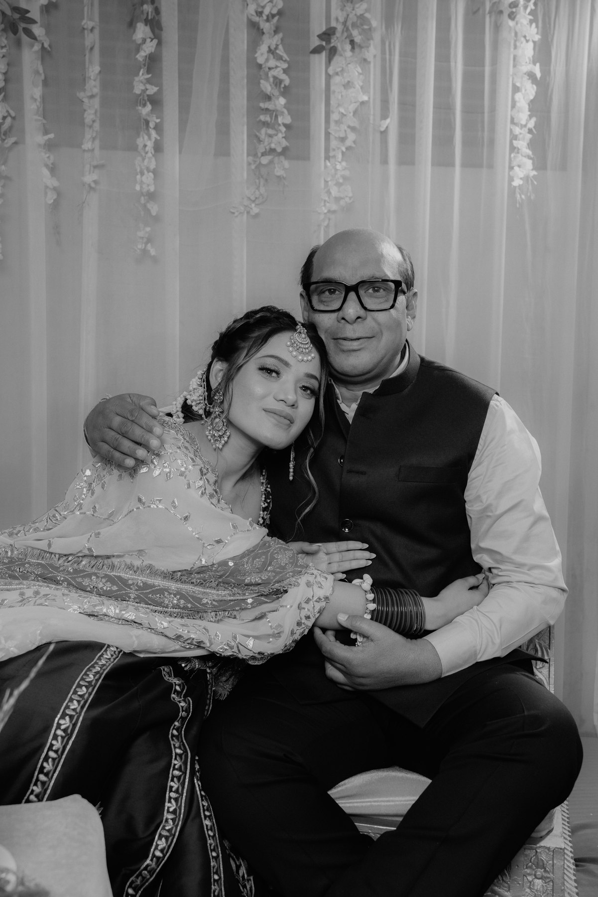 A black-and-white portrait of a bride resting her head on an older man's shoulder