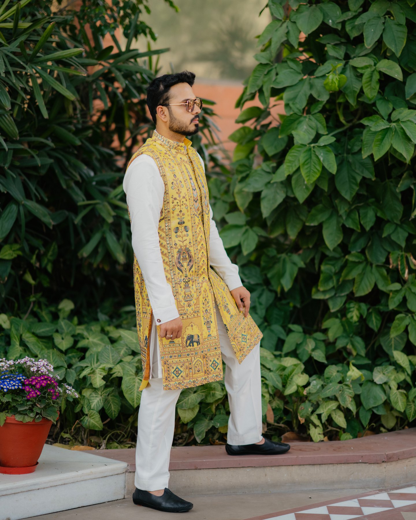 A groom in an embroidered yellow waistcoat beside green foliage